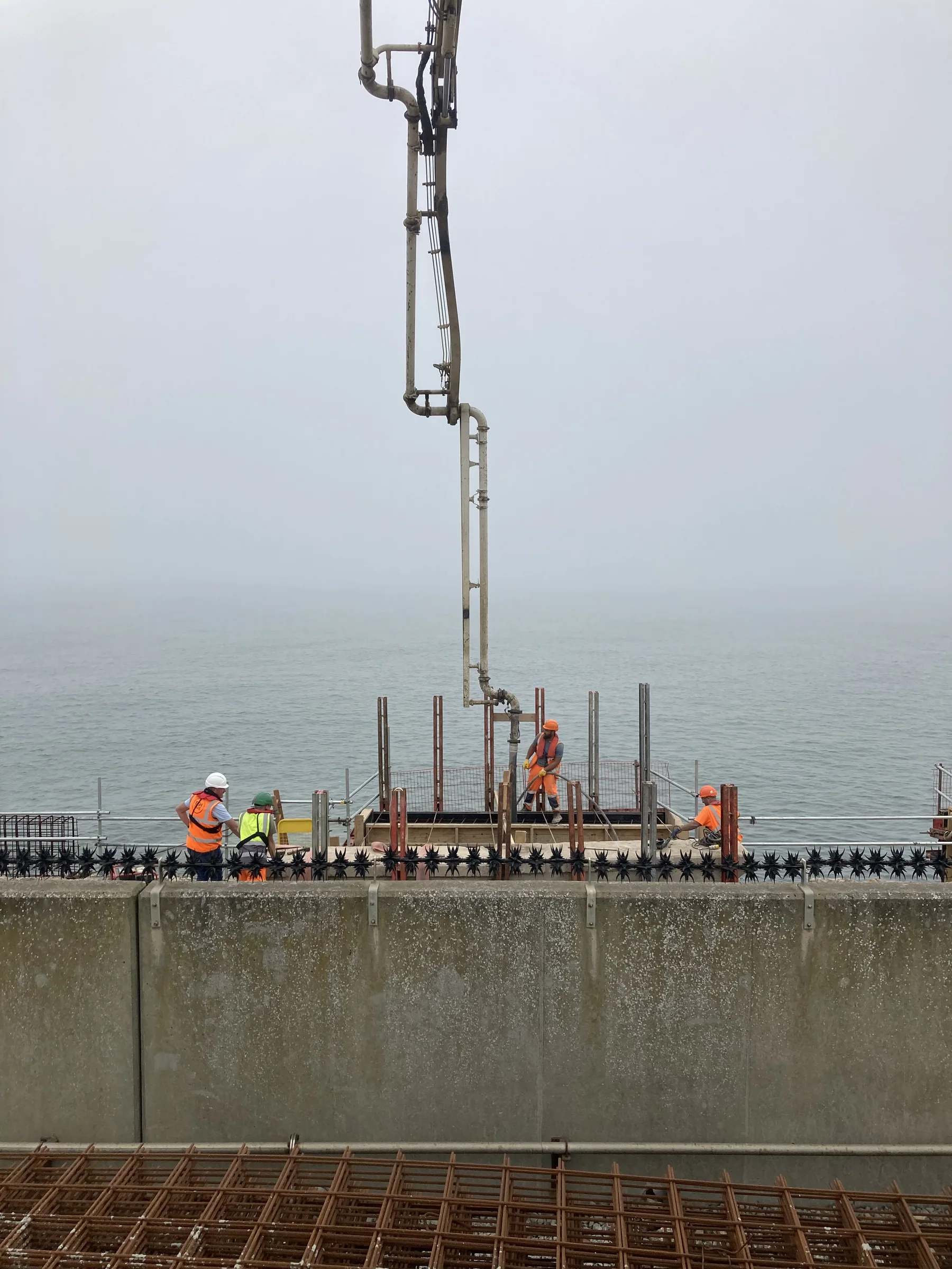 Site operatives placing pumped concrete into a prepared repair section beside the North Sea at Port of Sunderland.